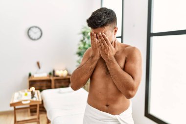 Genç İspanyol adam spa merkezinde üstsüz duruyor. Ağlarken suratını ellerle kapatıyor. depresyon kavramı. 