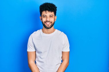 Sakallı, sıradan beyaz tişörtlü, yüzünde mutlu ve havalı bir gülümseme olan genç bir Arap. şanslı kişi. 