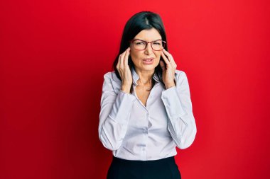 Genç İspanyol kadın iş gömleği ve gözlük takıp kulaklarını parmaklarıyla kapatıyor ve yüksek sesli müzik sesi için rahatsız edici bir ifade takınıyor. sağır kavramı. 