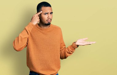 Genç Afro-Amerikalı bir adam günlük giysiler giymiş. Kafası karışmış ve avuç içi açık bir şekilde fotokopi alanı göstermekten rahatsız olmuş ve alnını işaret ediyor. Bunu bir düşün.. 