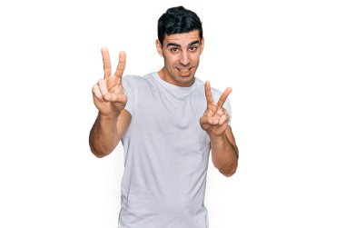 Beyaz tişört giyen yakışıklı İspanyol adam kameraya bakıp zafer işareti yaparken gülümsüyor. İki numara.. 