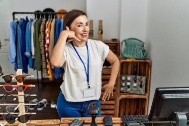 Güzel, orta yaşlı İspanyol bir kadın perakende mağazasında yönetici olarak çalışıyor. Gülümsüyor, telefonla el ve parmaklarıyla telefonla konuşuyor gibi yapıyor. iletişim kavramları. 