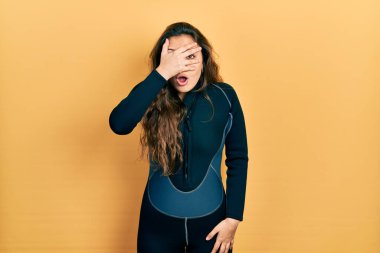 Genç İspanyol kız dalgıç neoprene üniforması giyiyor. Şoka girip yüzünü ve gözlerini kapıyor. Utanmış bir ifadeyle parmaklarından bakıyor.. 