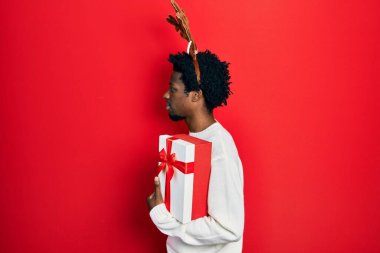 Geyik şapkası takan genç Afro-Amerikan bir adam. Yan tarafa bakıyor, rahat bir görünüm takınıyor ve kendine güvenen bir gülümseme takınıyor.. 
