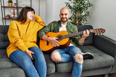 Genç İspanyol çift gülümseyerek evde kanepede oturmuş klasik gitar çalıyor..