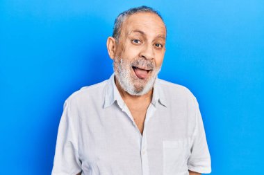 Sakallı, sıradan beyaz gömlekli yakışıklı, komik bir ifadeyle dilini dışarı çıkaran bir adam. duygu kavramı. 