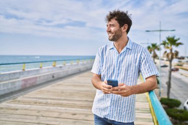 Genç İspanyol adam güvertede akıllı telefon kullanarak mutlu bir şekilde gülümsüyor..