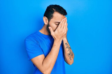 Sakallı, sıradan mavi tişörtlü, suratını elleriyle kapatıp ağlayan İspanyol bir adam. depresyon kavramı. 