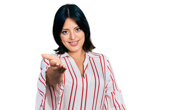 Молодая латиноамериканка, одетая в повседневную одежду, весело улыбается, протягивая руку помощи и принимая. 