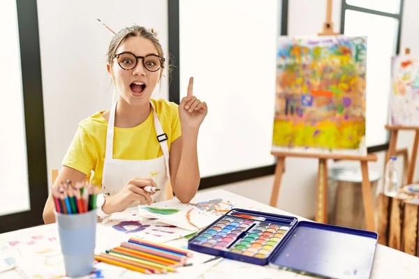 アートスタジオで若いブルネットのティーンエイジャーは 成功したアイデアで指を指しています 興奮して幸せよ 第1位 — ストック写真