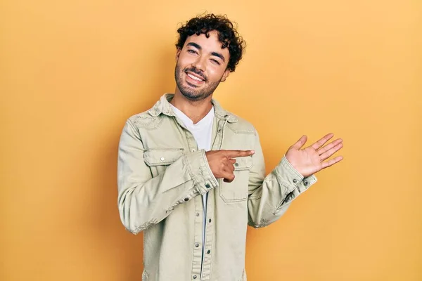 Mladý Hispánec Neformálním Oblečení Užaslý Usmívající Fotoaparátu Při Prezentaci Rukou — Stock fotografie