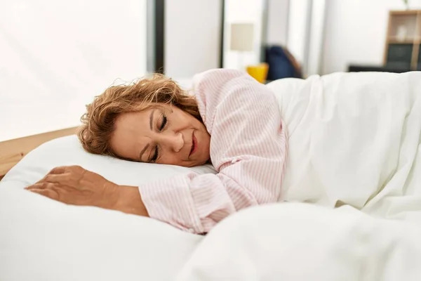 Middle age caucasian woman sleeping lying on the bed at bedroom.