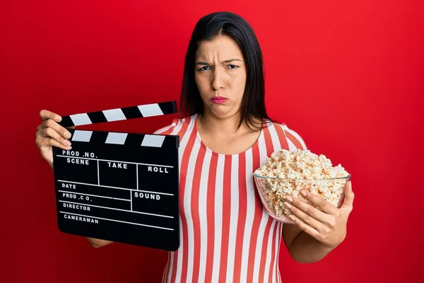 Młoda Latynoska Trzymająca Wideo Klapkę Popcorn Sceptyczna Nerwowa Marszcząca Brwi — Zdjęcie stockowe