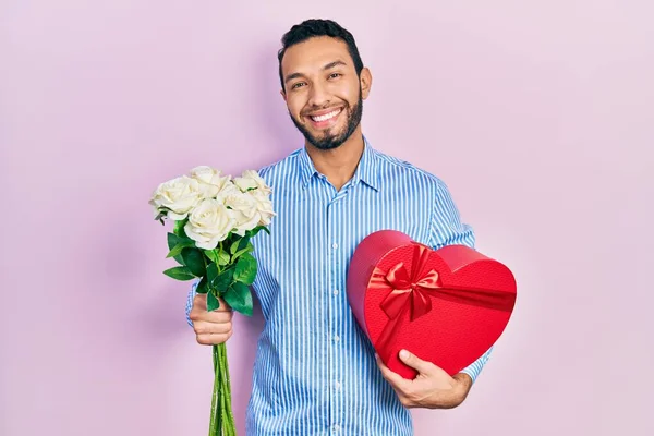 带着胡子的西班牙裔男人举着结婚周年礼物和一束鲜花 脸上挂着快乐而沉着的笑容 显示牙齿 — 图库照片