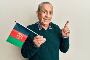 Gri saçlı yakışıklı son sınıf öğrencisi. Afgan bayrağı tutuyor. Gülümsüyor. 