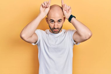 Genç kel adam, günlük beyaz t-shirt 'ler giyip parmaklarıyla boynuz gibi komik hareketler yapıyor. 