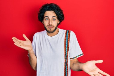 Sıradan beyaz tişörtler giyen yakışıklı İspanyol bir adam. Kolları ve elleri havada, kafası karışmış bir ifade. şüphe kavramı. 