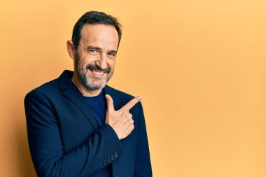 Orta yaşlı İspanyol bir adam iş kıyafetleri giyiyor. Gülümsüyor, eli ve parmağı yana doğru uzanıyor. 