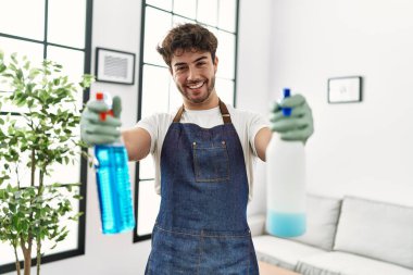 Genç İspanyol adam evde temizlik spreyi tutuyor.