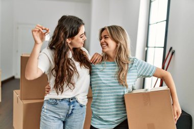 Mutlu bir şekilde gülümseyen genç çift yeni evin anahtarını ve karton kutuyu tutuyor..