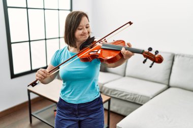 Down sendromlu esmer kadın oturma odasında keman çalışıyor.