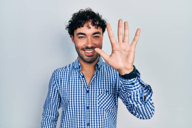 Gündelik kıyafetler giyen genç İspanyol adam beş numarayı gösterip işaret ederken kendinden emin ve mutlu bir şekilde gülümsüyor.. 