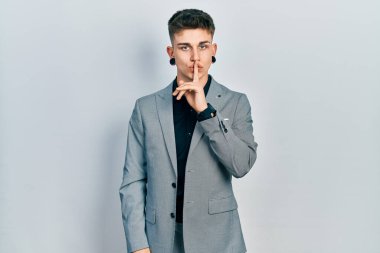 Kulakları genişlemiş, iş ceketi giymiş, dudakları parmaklarıyla sessiz olmak isteyen beyaz bir çocuk. sessizlik ve gizli konsept. 