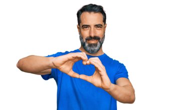 Orta yaşlı, sakallı, sıradan mavi tişörtlü aşık gülümseyen, elleriyle kalp sembolü yapan bir adam. romantik kavram. 