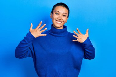 Kısa saçlı, balıkçı yaka kazak giyen güzel İspanyol kadın parmaklarıyla on numarayı gösterirken kendinden emin ve mutlu gülümsüyor.. 