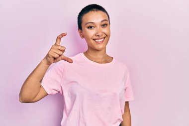 Kısa saçlı, sıradan pembe tişörtlü, güzel İspanyol bir kadın gülümseyen, kendine güvenen, el hareketi yapan, parmaklarıyla işaret yapan ve kameraya bakan. ölçüm kavramı. 