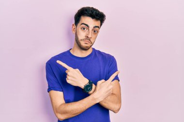 Gündelik tişört giyen genç İspanyol adam iki tarafı da parmaklarıyla işaret ediyor, farklı yönlerde. 