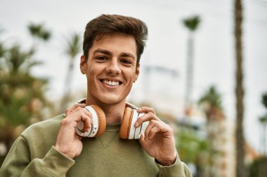 Şehirde kulaklık takarak mutlu gülümseyen genç İspanyol adam..