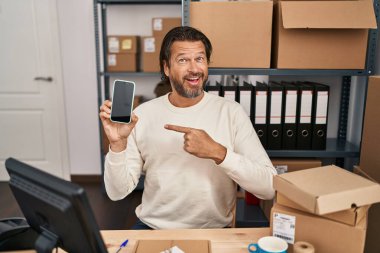 Küçük işletme şirketinde çalışan yakışıklı orta yaşlı bir adam elinde akıllı bir telefonla mutlu bir şekilde el ve parmak işareti yapıyor. 