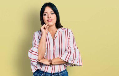 Gündelik kıyafetler giyen genç İspanyol kız kameraya kendinden emin bakıyor kollarını kavuşturup gülümsüyor ve çenesini kaldırıyor. Olumlu düşünmek. 