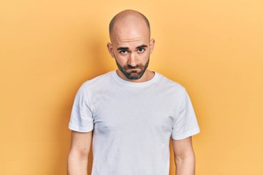 Gündelik beyaz tişört giyen, kuşkucu ve gergin genç kel bir adam sorun yüzünden surat asıyor. negatif kişi. 