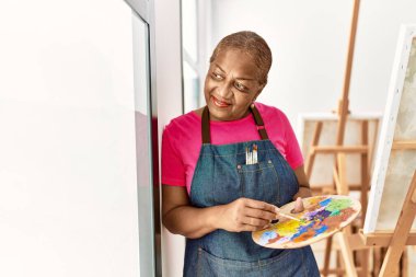 Kıdemli Afro-Amerikan kadın sanat stüdyosunda kendine güvenerek gülümsüyor.