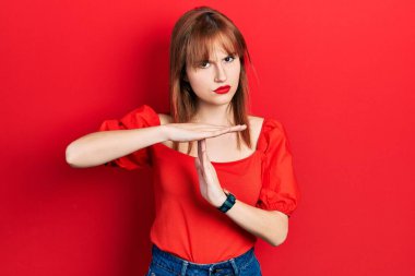 Kırmızı tişörtlü kızıl saçlı genç bir kadın. Elleriyle jest yapıyor, hayal kırıklığına uğramış ve ciddi bir yüz ifadesi takınıyor. 