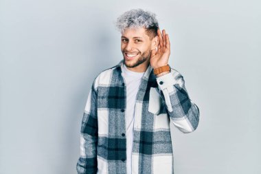 Modern boyalı saçlı, sıradan tişörtlü, ağzı kulaklarında, dedikoduları ve dedikoduları dinleyen genç İspanyol bir adam. Sağırlık kavramı. 