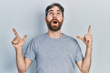 Gri tişörtlü, beyaz sakallı bir adam şaşkın şaşkın yukarı bakıyor ve parmaklarıyla işaret ediyor ve kollarını kaldırıyordu.. 