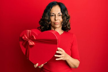 Orta yaşlı İspanyol kadın elinde sevgililer günü hediyesi tutarken düşünceli tavır takınıyor ve kendinden emin görünüyor. 