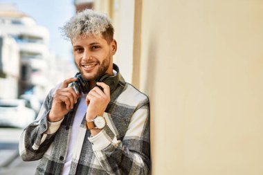 Şehirde kulaklık takarak mutlu gülümseyen genç İspanyol adam..