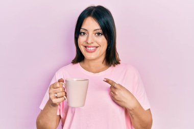 Bir fincan kahve içen genç İspanyol kadın mutlu bir şekilde el ve parmağıyla işaret ediyor. 