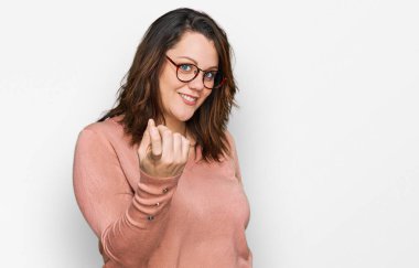 Genç ve cüsseli bir kadın günlük kıyafetler ve gözlük takıyor. Buraya el hareketleriyle mutlu bir şekilde karşılamaya ve gülümsemeye davet ediyor. 