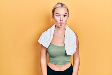 Spor kıyafetleri ve havlu giyen genç sarışın kız dudaklarıyla balık suratı yapıyor, çılgınca ve komik bir jest. Komik ifade. 