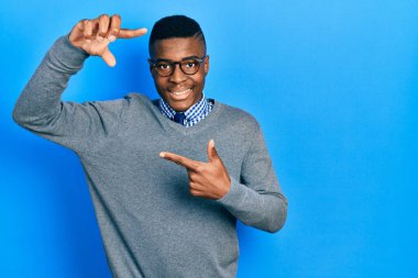 İş stili ve gözlüklü genç Afro-Amerikan adam gülümsüyor. Elleriyle ve parmaklarıyla gülen yüzüyle çerçeve yapıyor. yaratıcılık ve fotoğrafçılık kavramı. 