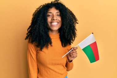 Afro saçlı Afro-Amerikalı kadın elinde madagaskar bayrağı tutuyordu. Olumlu ve mutlu görünüyordu. Kendine güvenen bir gülümsemeyle dişlerini gösteriyordu. 