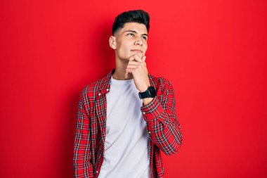 Elleri çenesinde gündelik giysiler içinde soru soran genç İspanyol bir adam, düşünceli bir ifade. Düşünceli bir yüzle gülümsüyor. şüphe kavramı. 