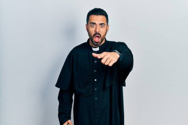 Sakallı yakışıklı, Katolik rahip cübbesi giyen yakışıklı bir adam kameraya kızgın ve sinirli bir şekilde bakıyor. 
