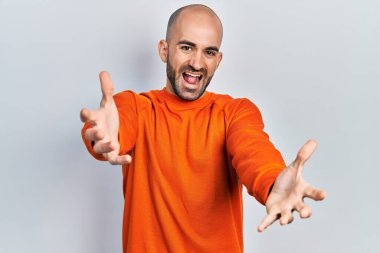 Sıradan kıyafetler giyen genç kel adam kameraya sarılıp gülümseyerek gülümsüyor. Mutluluğu kucaklayan neşeli bir ifade.. 