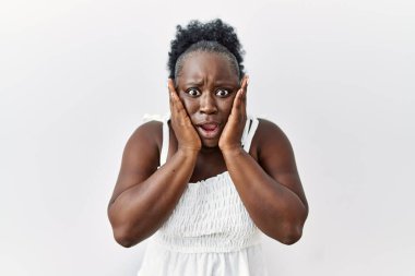 Beyaz arka planda duran genç Afrikalı kadın korkmuş ve şok olmuş, şaşırmış ve hayretler içinde kalmış. 